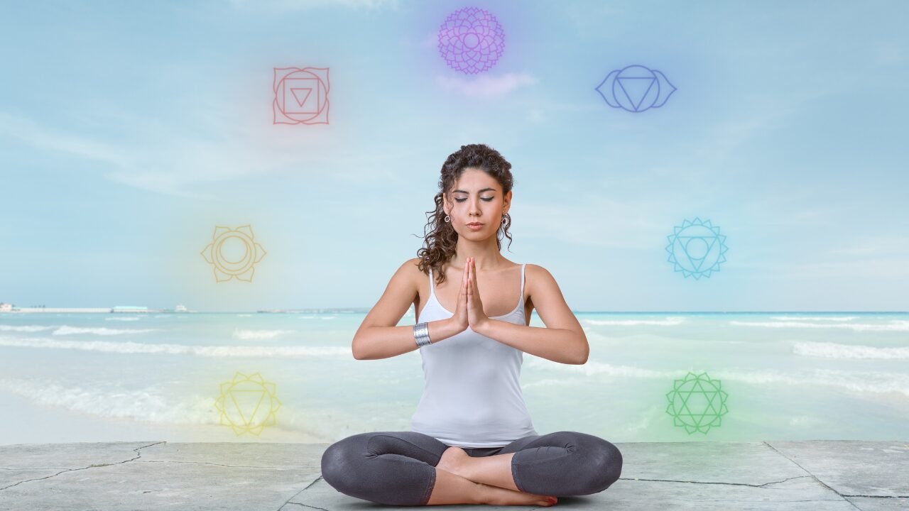 Image of a woman seated in a yoga posture with chakra symbols surrounding her, representing chakra balance during meditation.